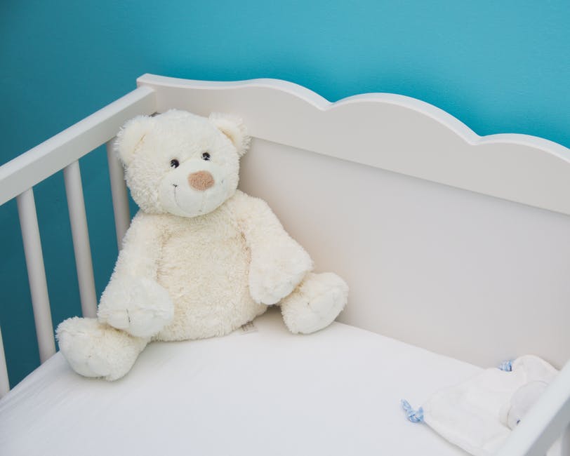 An image showing a white teddy bear in a white baby cot with blue walls